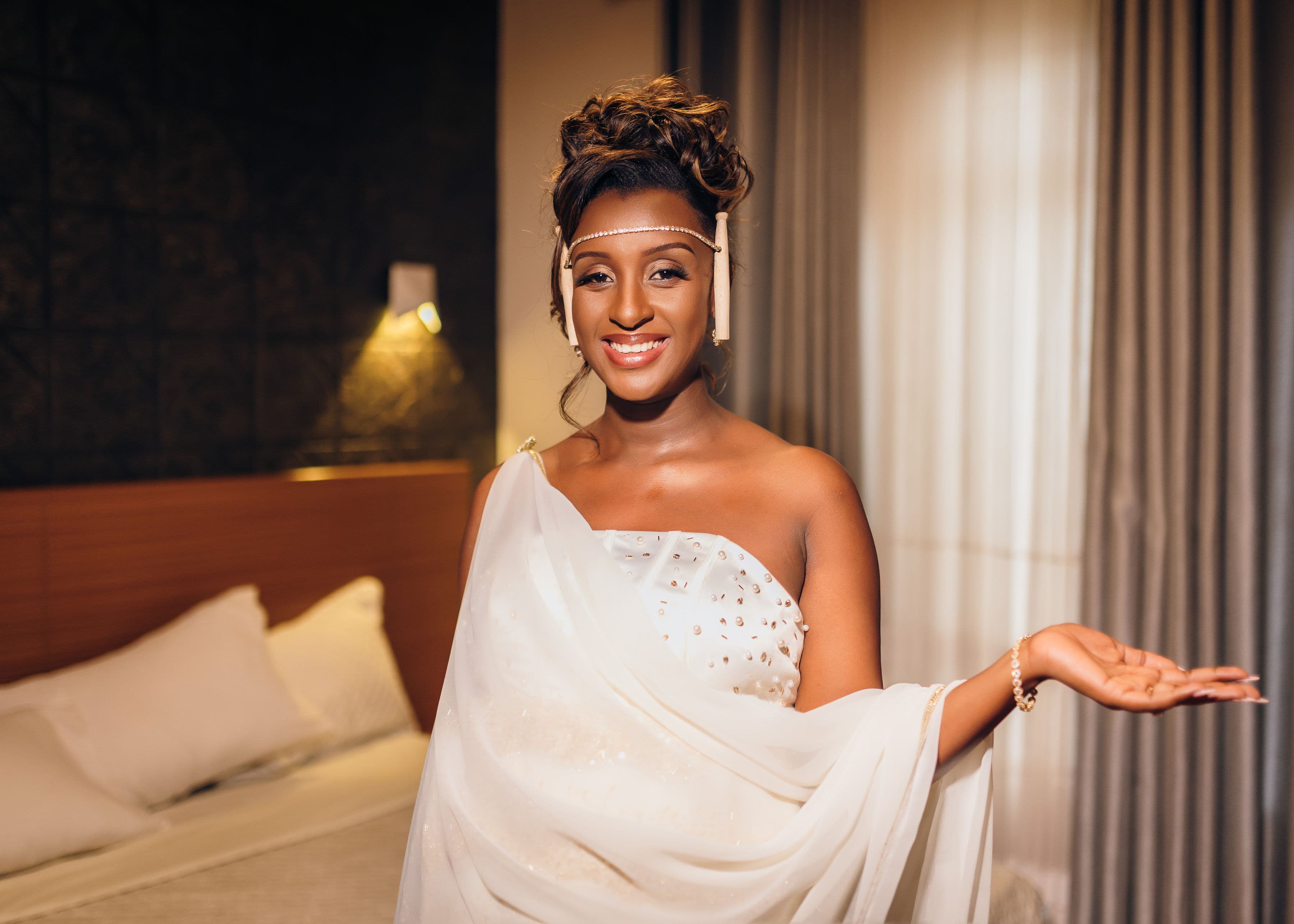 Mwanamke anayetabasamu akiwa amevaa vazi jeupe la kitamaduni la Rwanda na taji la kichwani.