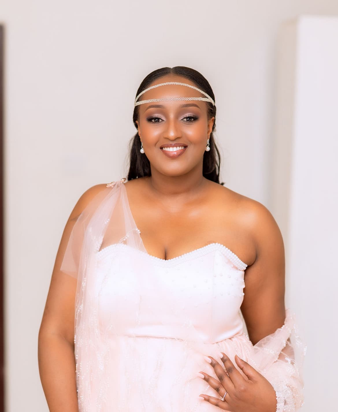 Mwanamke anayetabasamu akiwa amevaa rinda la pinki lenye lulu na taji maridadi ya fedha.